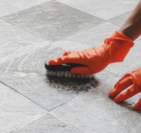 Person wearing rubber gloves cleaning grey floor tiles with brush