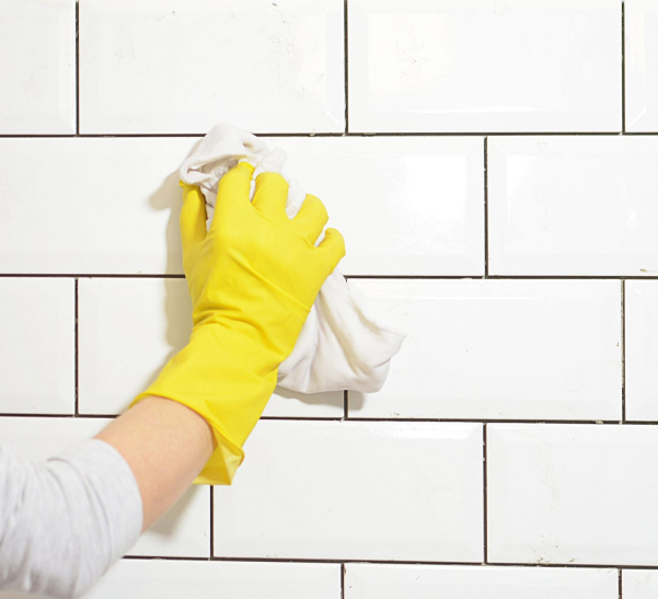 Person wearing rubber glove wiping white wall tile with towel