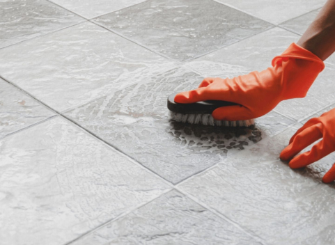 Person wearing rubber gloves cleaning grey floor tiles with brush