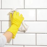 Person wearing rubber glove wiping white wall tile with towel