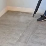 Person using a steam cleaner on wood-look tiles, demonstrating professional tile and grout cleaning in a home setting.